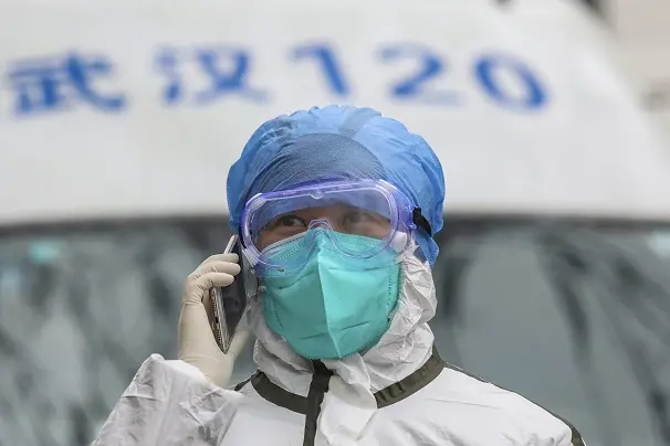 In this Sunday, Jan. 26, 2020 photo, a nurse in protective gear talks on her phone near an ambulance in Wuhan in central China\\'s Hubei Province. A new viral illness being watched with a wary eye around the globe accelerated its spread in China on Sunday with 56 deaths so far, while the U.S. Consulate in the city at the epicenter announced it will evacuate its personnel and some private citizens aboard a charter flight. (Chinatopix via AP)