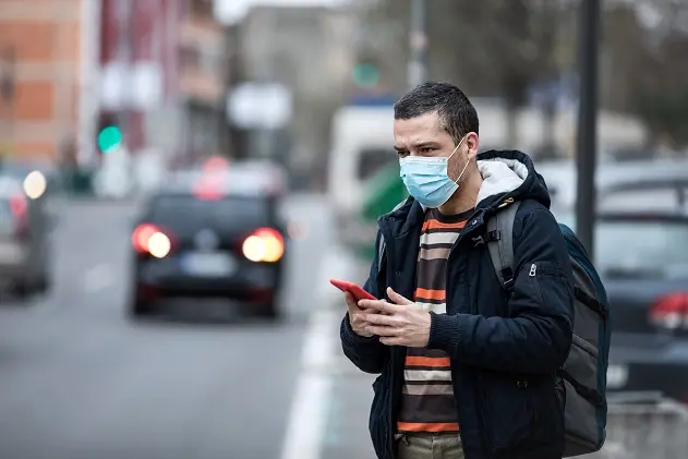 Coronavirus protection. Mature  man in the city after the work day, wearing protective mask on the face. Calling for a taxi.
