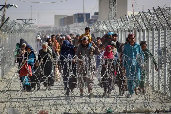 TOPSHOT - Afghans walk along fences as they arrive in Pakistan through the Pakistan-Afghanistan border crossing point in Chaman on August 24, 2021 following Taliban\\'s military takeover of Afghanistan. (Photo by - / AFP)