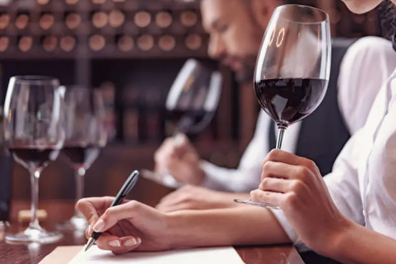Two sommeliers, male and female tasting red wine and making notes at degustation card