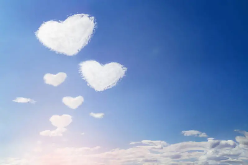 Fluffy clouds forming a hearts shape on blue sky with sun, soft focus. Heavenly clouds background. Valentine day, love, romantic, Mother day concept. Copy space. Empty place for message.