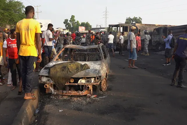 epaselect epa09567869 Sierra Leone residents of Freetown look at burned vehicles in the aftermath of an explosion at a junction outside Choithram Supermarket in Freetown, Sierra Leone, 06 November 2021.  At least 99 people have died following a massive fuel tanker explosion in the capital Freetown, after a fuel tanker collided with a truck.  EPA/MOHAMED KONNEH