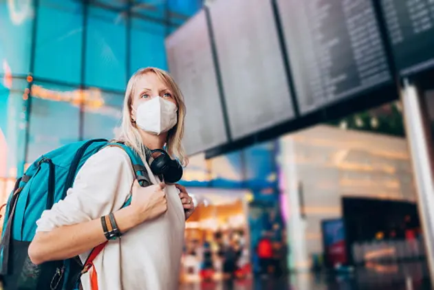 Portrait of a young woman checks the arrivals and departures board at the airport. She wears a face mask for protection during a Coronavirus pandemic.\\r\\nNew normal lifestyle for public transport after Covid-19