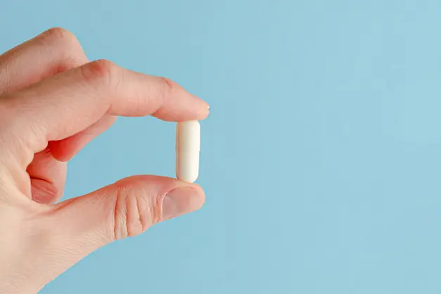 Female hand holding white capsule on blue background. Close, copy space. Medicine concept