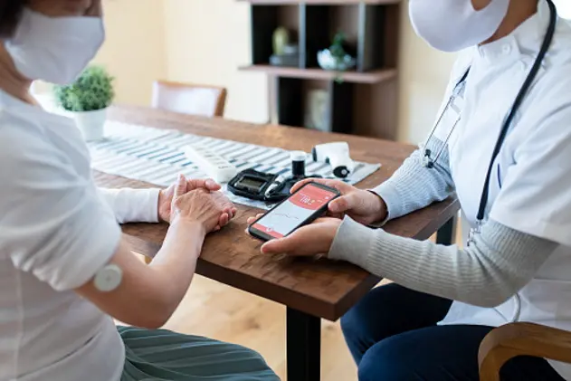 Doctor talking to an elderly patient and using a smartphone app to check patients blood sugar levels at home. Okayama, Japan.