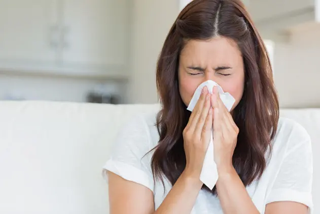 Brunette sneezing in a tissue in the living room