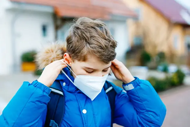 Kid boy wearing ffp medical mask on the way to school. Child backpack satchel. Schoolkid on cold autumn or winter day with warm clothes. Lockdown and quarantine time during corona pandemic disease.