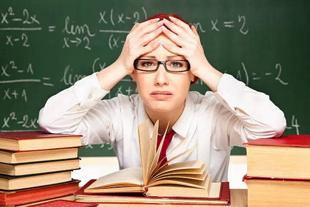 \"Beautiful young teacher in a classroom, sitting behind her desk, with a desperate look on her face\"