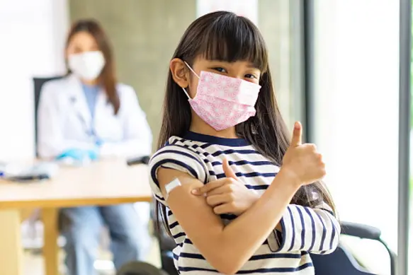 Asian  doctor wearing gloves and isolation mask is making a COVID-19 vaccination in the shoulder of child patient  at hospital.