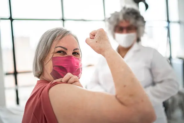 Woman being vaccinated and flexing biceps muscle - wearing face mask