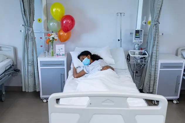 Mixed race sick girl lying in hospital bed wearing face mask and fingertip pulse oximeter. medicine, health and healthcare services during coronavirus covid 19 pandemic.