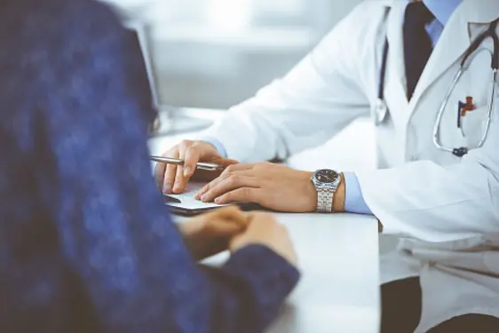 Unknown young woman patient discuss the results of her medical tests with a doctor, while sitting at the desk in a hospital office. Physician using clipboard for filling up medication history records. Perfect medical service in clinic. Medicine and healthcare concepts.