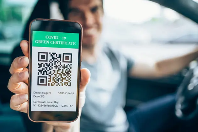 Defocused young man sitting in his car and showing smartphone with valid digital vaccination certificate for COVID-19. Focus is on the phone.