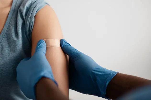 Vaccination of patients in hospital against covid-19 pandemic. Hands of african american doctor in protective gloves puts band aid to inculcate site to patient in clinic, close up, free space, cropped