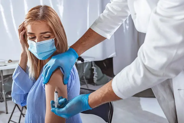 Photo up male doctor holding syringe, injection to female patient in medical mask. Covid-19 or coronavirus vaccine.