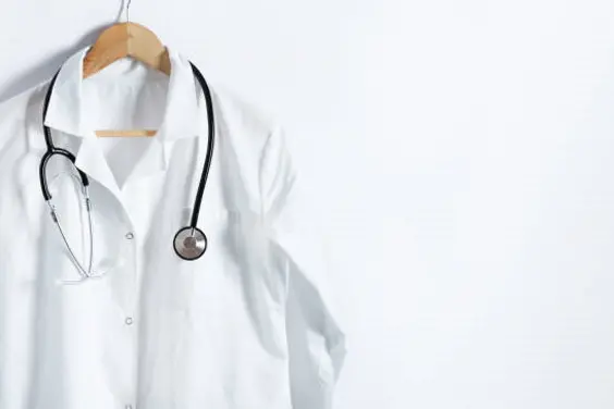 Doctor\\'s white coat with stethoscope on hanger over white background with copy space. Healthcare and medical concept.