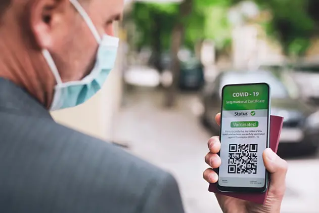 Businessman with protective face mask showing International Certificate of Covid-19 vaccination and passport. Mobile app.