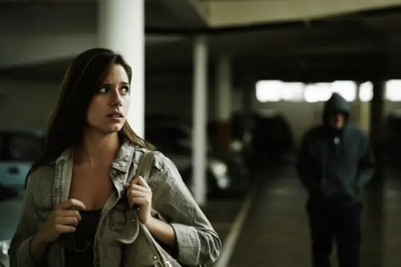 A terrified young woman in an underground parking garage being followed by a sinister man