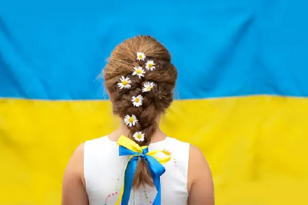 A girl with daisies in a braid and a yellow and blue ribbon against the background of the flag of Ukraine. Independence Day of Ukraine, Flag Day, Constitution Day