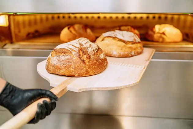 Baker putting bread in the bakery oven cowering on the floor of the bakery