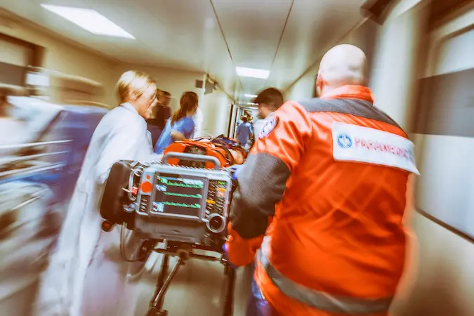 Paramedics and female doctor pulling hospital trolley.