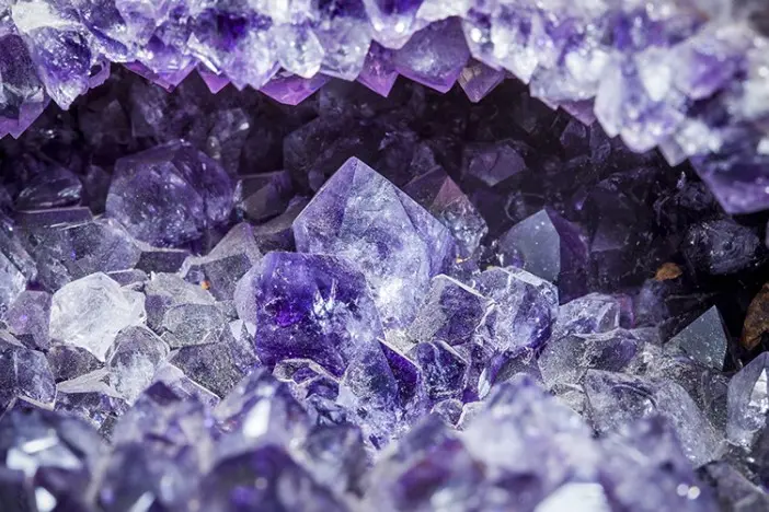 Horizontal close up still of inside the cave of large purple amethyst crystal geode cluster sparkling with raw rock edges