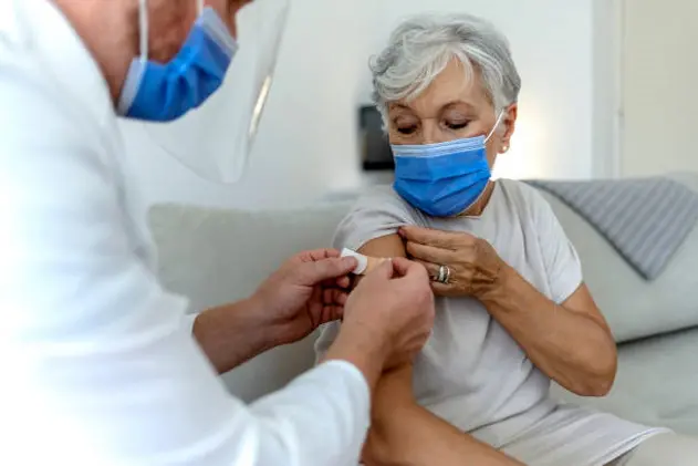 A male doctor puts a band aid on a senior woman\\'s arm after he administered the COVID-19 vaccine injection. Close up image of elderly woman having vaccination. Coronavirus, medical exam, consultation.