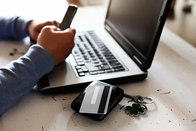 Human hands holding mobile phone in front of laptop computer