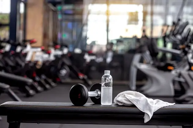 Dumbbell, water bottle, towel on the bench in the gym.