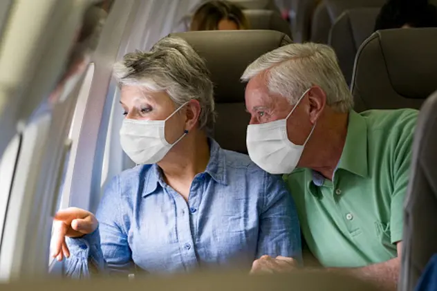 Latin American senior couple traveling by plane wearing facemasks and looking through the window - travel during the COVID-19 pandemic