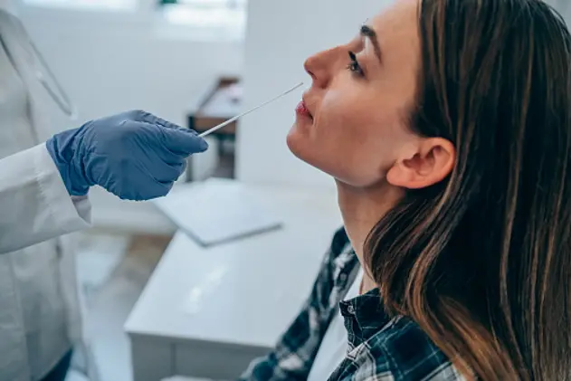 Shot of a doctor using cotton swab while doing coronavirus PCR test at the hospital. Doctor laboratory assistant takes swab from nose of sick patient. Unrecognizable doctor with protective glove taking coronavirus sample from female patient\\'s nose.