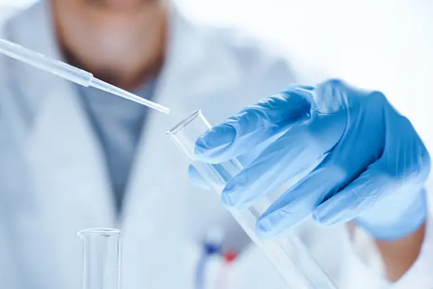 Microbiological research with a test tube and micropipette in hands of a laboratory worker in close-up