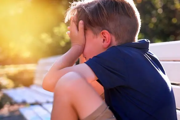 Crestfallen Crying child boy sitting on a bench covering his face