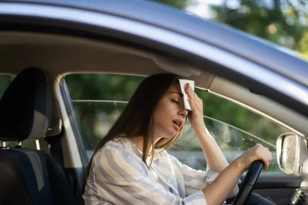 Girl driver being hot during heat wave in car, suffering from hot weather, has problem with a non-working air conditioner, wipes sweat from her forehead with tissue. Summer, heat concept.