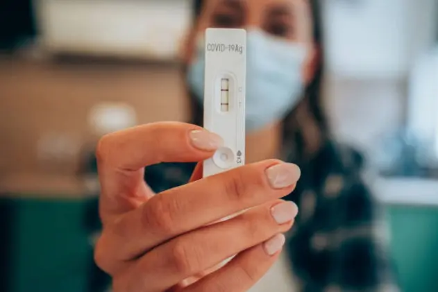 Close-up shot of doctor\\'s hand with protective gloves holding a positive test device to senior patient. Doctor documented the result after a positive test. Doctor hand holding positive Coronavirus/Covid-19 rapid test. Focus is on the test.