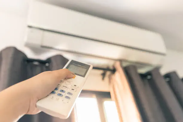 The girl\\'s hand is using a remote control to turn on the air conditioning in the room during the summer.