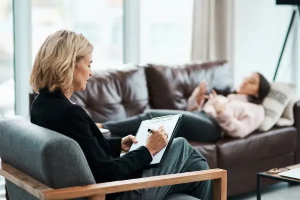 Shot of a mature psychologist writing notes during a therapeutic session with her patient