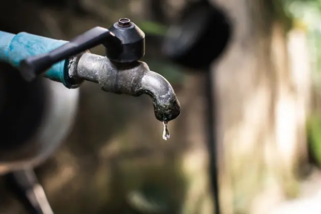 Old faucet with water leaking drop to the ground.