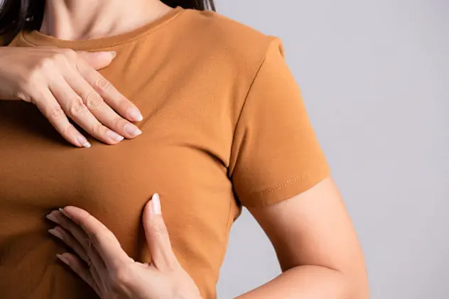 Woman hand checking lumps on her breast for signs of breast cancer on gray background. Healthcare concept.