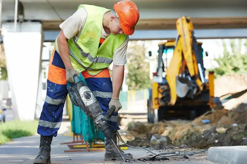 Builder worker with pneumatic hammer drill equipment breaking asphalt at road construction site