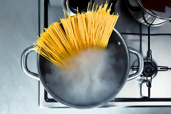 Cooking raw spaghetti in the boiling water contained in a saucepan. Italian cuisine. Raw food. interior of a domestic kitchen. Food preparation and cooking