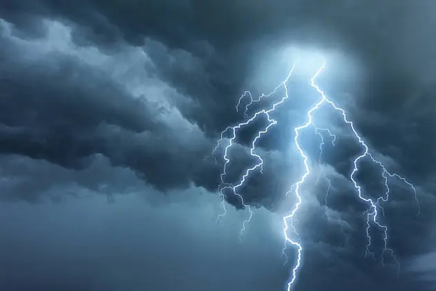 Bright lightning illuminates dark cloudy sky during a thunderstorm. Natural dangers and majestic beauty. Real cloudscape with computer generated lightning. Copy space on image side.