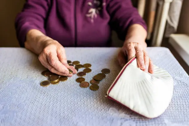 Concerned elderly woman sitting at home and counting remaining coins.old woman sitting miserably at the table at home and counting remaining coins from the pension in her wallet after paying the bills