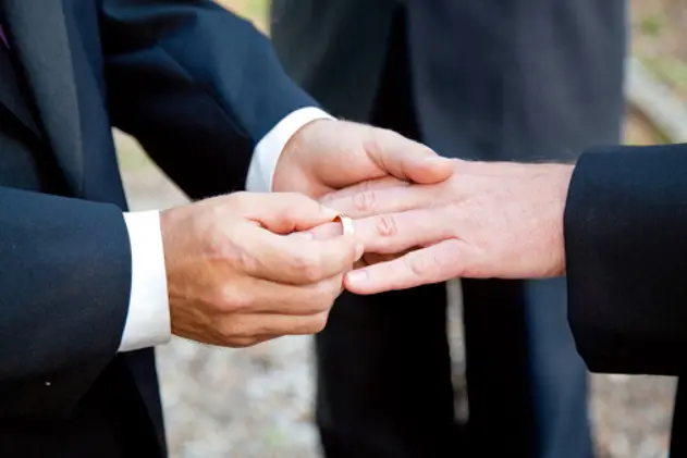 One groom placing the ring on another man\\'s finger during gay wedding.