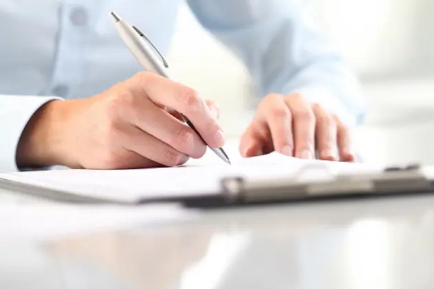 Woman\\'s hands writing on sheet in a clipboard with a pen; isolated on desk