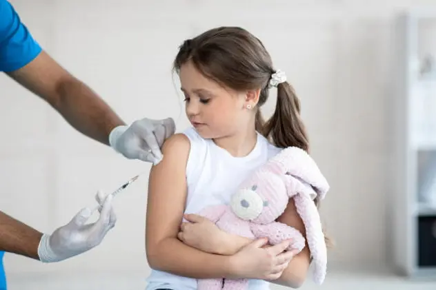 Doctor doing injection of coronavirus vaccine to little girl with toy bunny at clinic. Cute child on visit to medical specialist, getting immunization against coronavirus. Medicine and vaccination