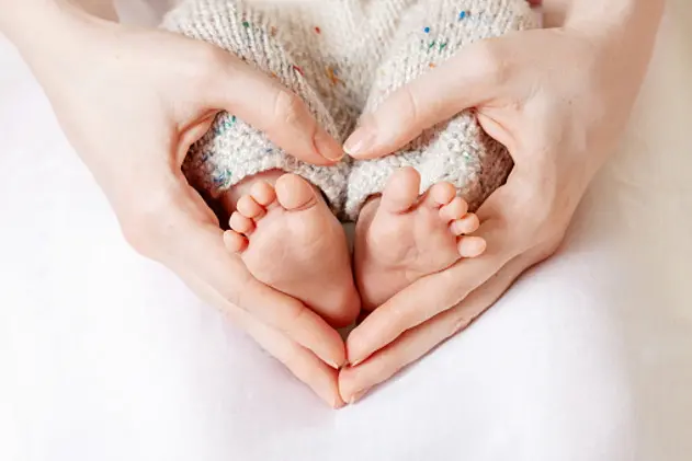 Baby feet in mother hands. Tiny Newborn Baby\\'s feet on female Heart Shaped hands closeup. Mom and her Child. Happy Family concept. Beautiful conceptual image of Maternity