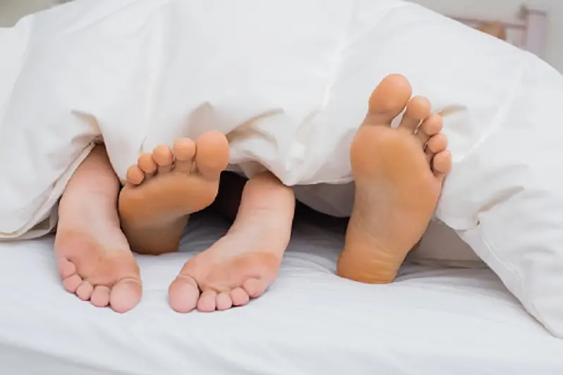 Two pairs of feet under the covers at home in bedroom