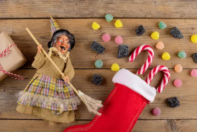 The witch Befana and red stocking with sweet coal and candy on rustic wooden background. Italian Epiphany day tradition, top view, flat lay, greeting card