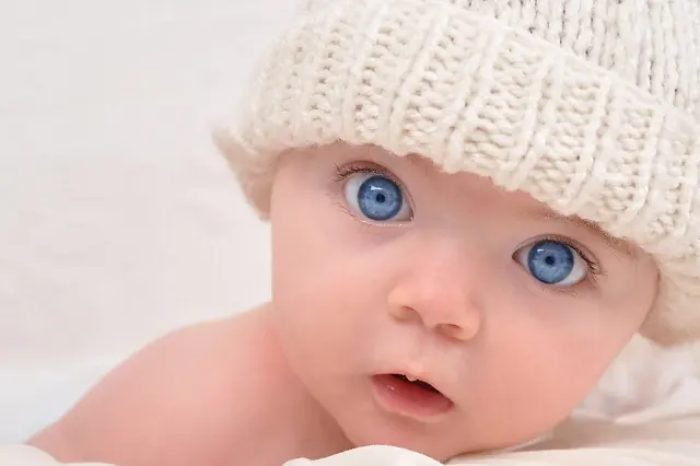 A cute little baby is looking into the camera and is wearing a white hat. The baby could be a boy or girl and has blue eyes. use it for a parenting or love concept.; Shutterstock ID 62715262; PO: novembre